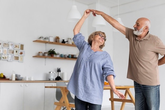 Casal de pessoas com aproximadamente 60 anos dançando na cozinha.