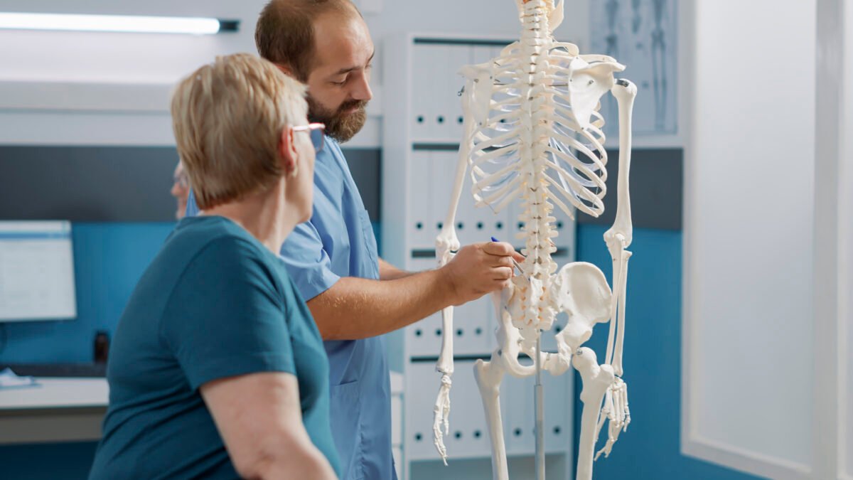 Especialista em coluna mostrando num esqueleto para sua paciente onde fica a dor em que ela está sentindo.