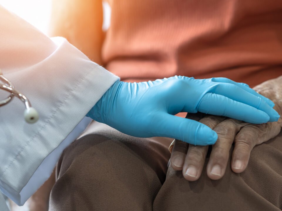 Imagem de paciente com Parkinson e neurologista com sua mão sob a da paciente, como uma forma de mostrar que a profissional está ali para ajudá-la.