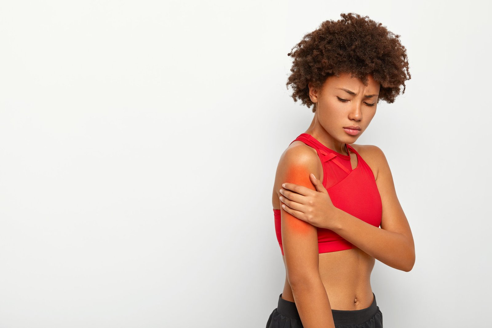 fotografia de mulher com roupa de ginástica, ela está com a mão na parte superior do braço, que está com uma mancha vermelha, criada por computador. Pode ser sintoma da mialgia.