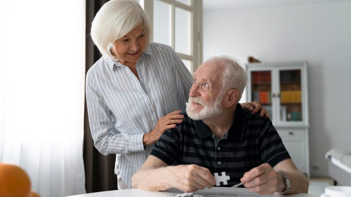 Casal de idosos, em que ambos estão lidando com os estágios do Parkinson. Eles estão montando joguinhos quebra-cabeça para manter-se em atividade cerebral e motora.