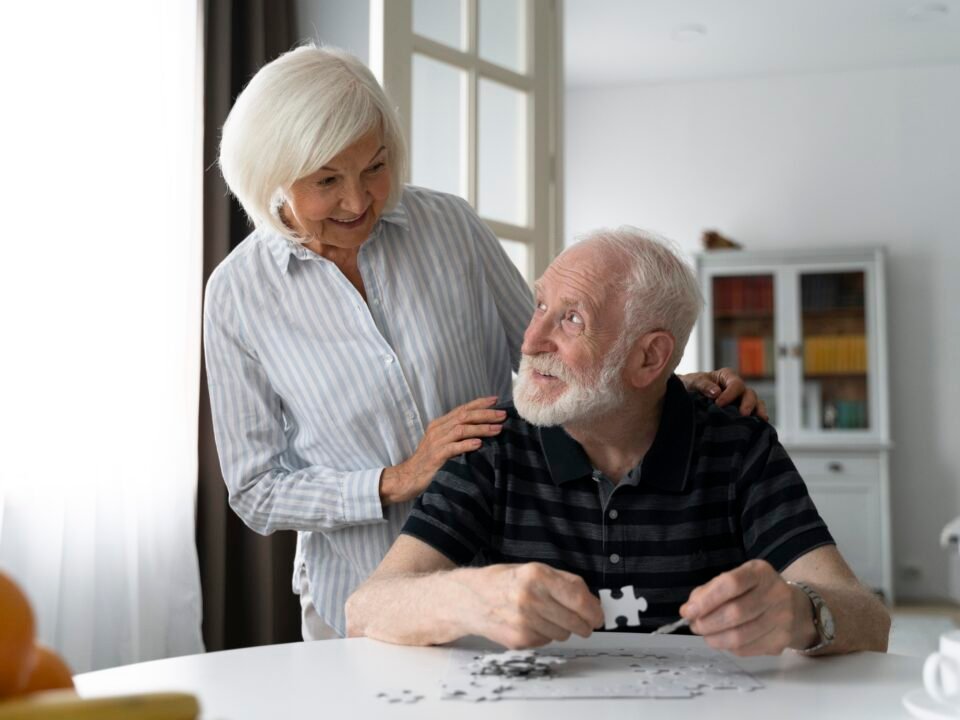 Casal de idosos, em que ambos estão lidando com os estágios do Parkinson. Eles estão montando joguinhos quebra-cabeça para manter-se em atividade cerebral e motora.