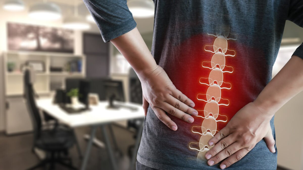 Fotografia de homem com as mãos na coluna, mais especificamente na lombar. Há uma coluna em 3D em cores branca e vermelha.