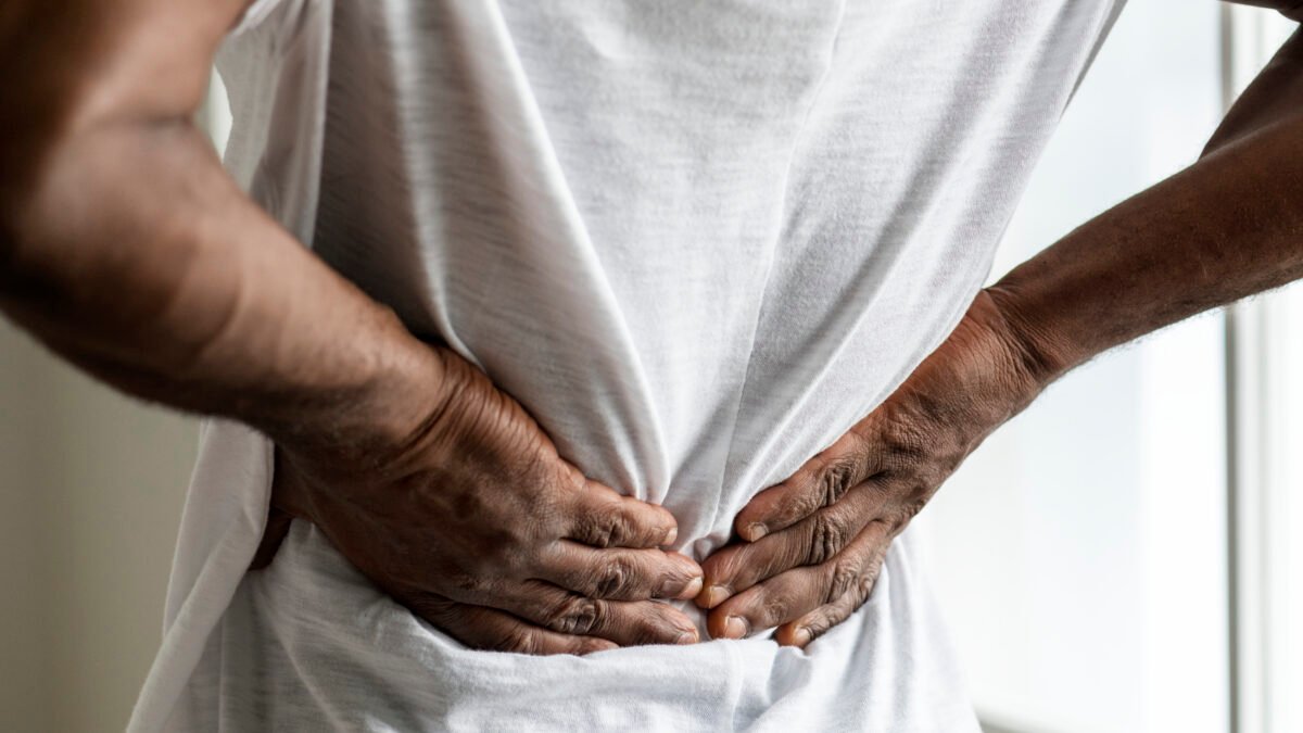 Fotografia de homem com as mãos na coluna indicando dor, ele pode estar com diagóstico de osteofitose.