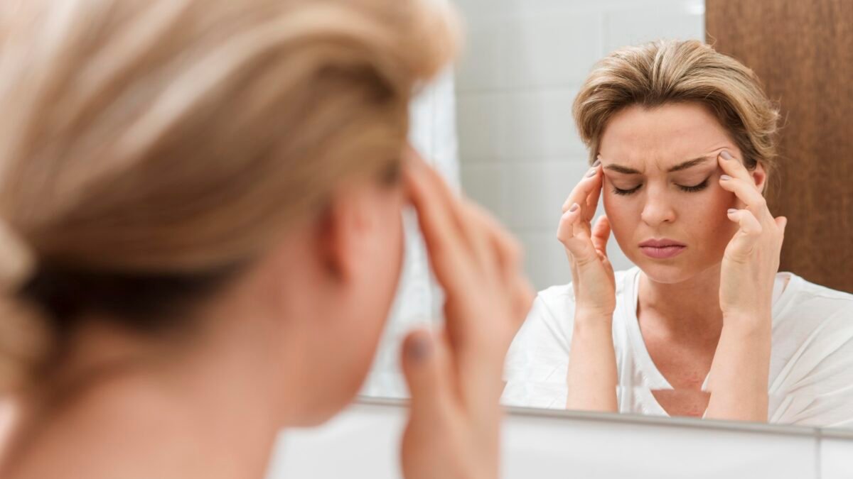 Fotografia de mulher com paralisia facial com os olhos fechados na frente do espelho.