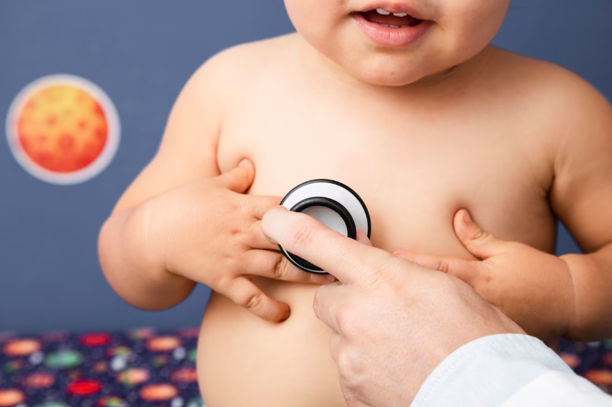 Fotografia de médico examinando o paciente, que pode estar com problemas de coração devido ao não tratamento da síndrome de Crouzon. A imagem mostra apenas a mão do médico no estetoscópio ouvindo o coração do bebê, que está confortável com a ação.