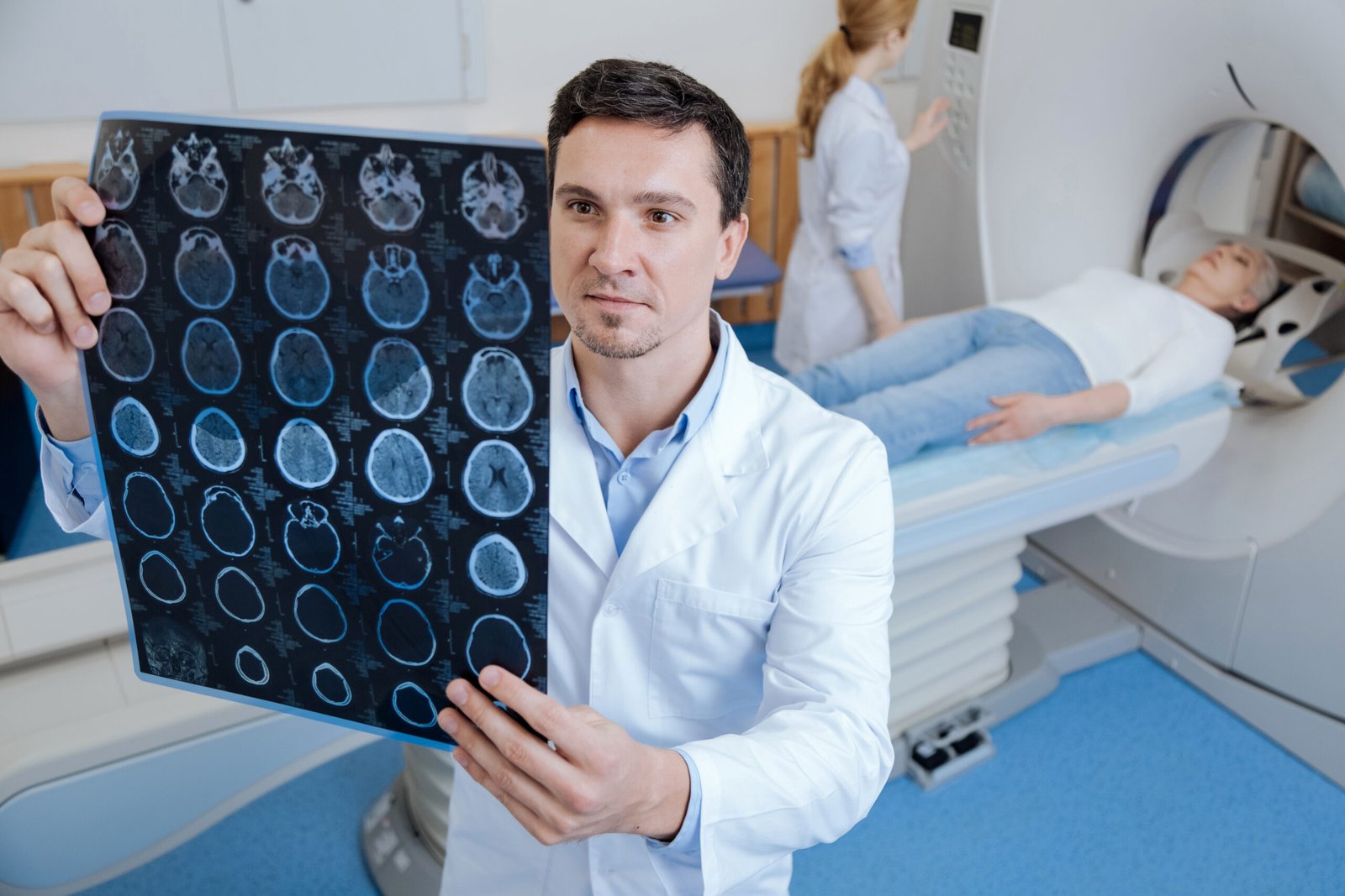 Fotografia de paciente realizando exame de imagem craniana. Ela está deitada no local apropriado para o exame enquanto o neurologista examina as imagens do cérebro.