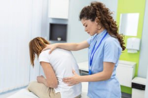 Imagem de profissional da saúde ajudando uma paciente que, por estar com dor na coluna, se posiciona com corcundez.