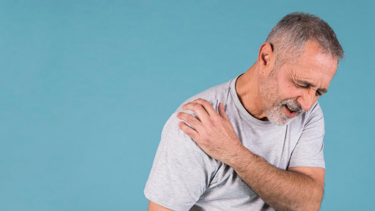 Imagem de homem com aproximadamente 60 anos com a mão no ombro, com expressão de dor.