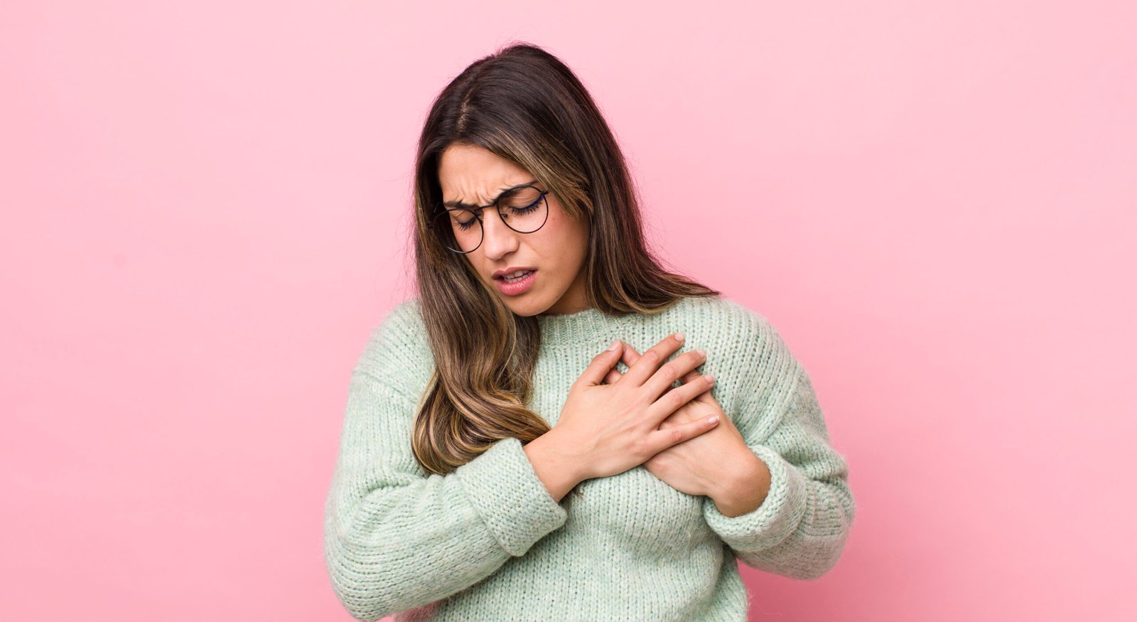 Fotografia de mulher com as duas mãos no peito, sintoma comum de infarto. O infarto está entre as causas da mão dormente.