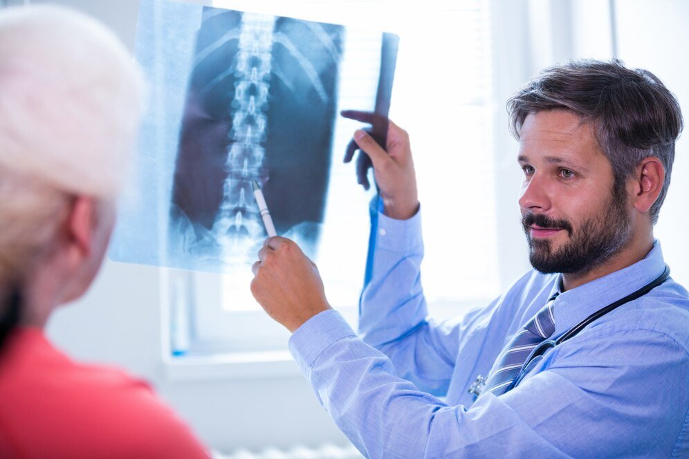 Foto de um médico homem, vestindo camisa social azul e gravata azul, que segura um raio-x da coluna para avaliação da realização de artrodese cervical.